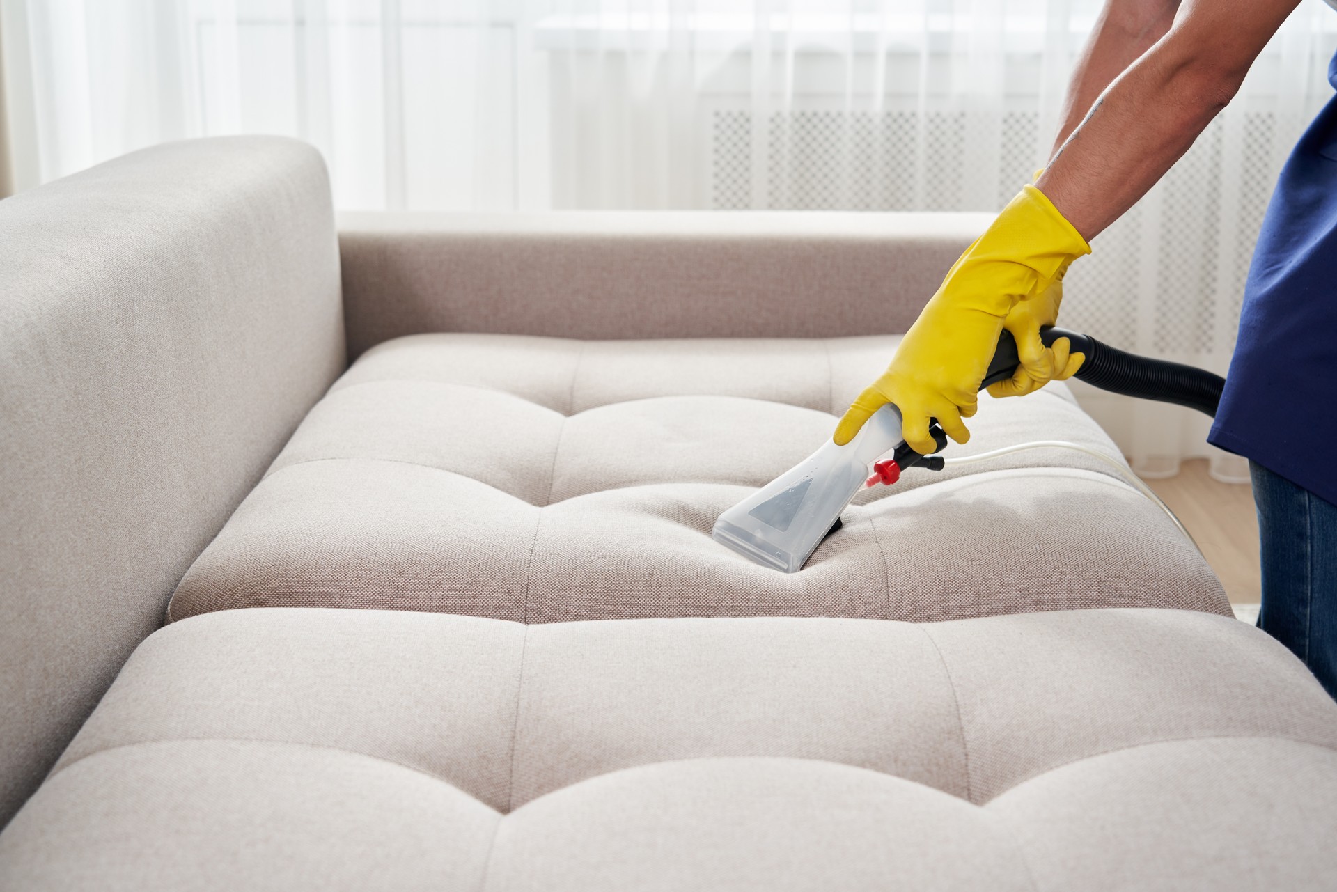 Close-up of housekeeper holding modern washing vacuum cleaner and cleaning dirty sofa with professionally detergent. Professional springclean at home concept